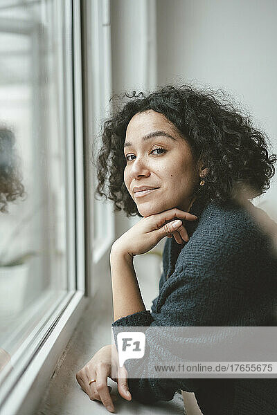 Beautiful woman with curly hair standing by window at home