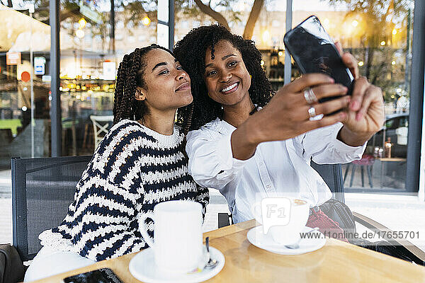 Smiling colleagues taking selfie through smart phone at sidewalk cafe