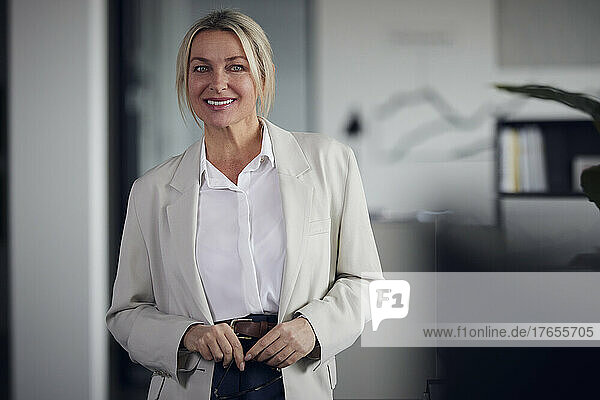 Lächelnde Geschäftsfrau mit blonden Haaren  die im Büro steht