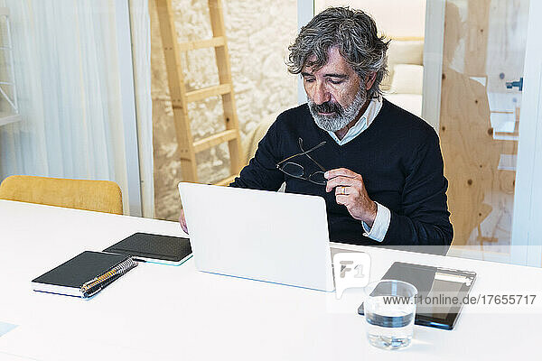 Freelancer holding eyeglasses using laptop working from home