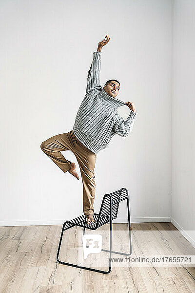 Man with hand raised balancing on chair in front of wall