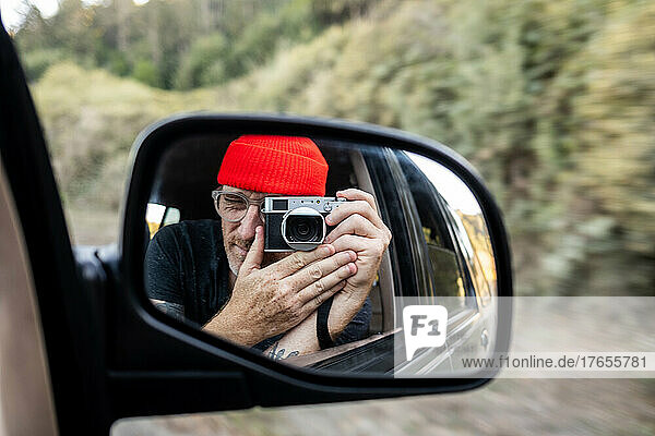 Person taking self portrait in rearview mirror of car while driving
