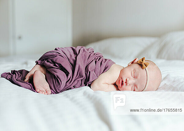 newborn baby girl covered in a swaddle laying on a white bed