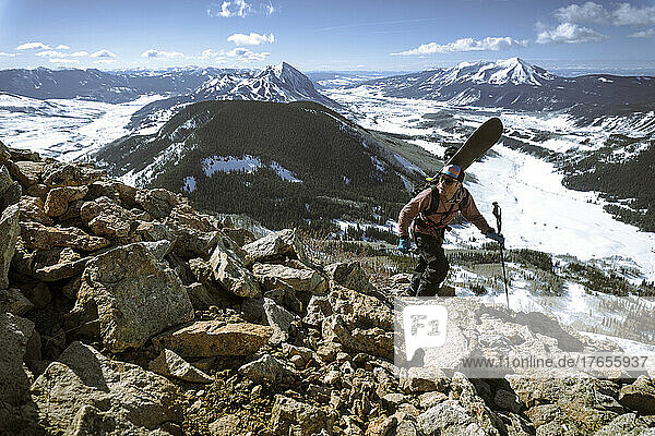 An adventurer climbing a mountain carrying a snowboard