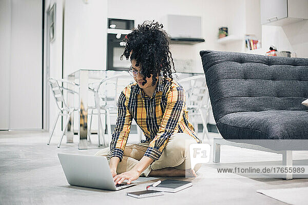 young Afro woman working from home sitting on floor with her laptop
