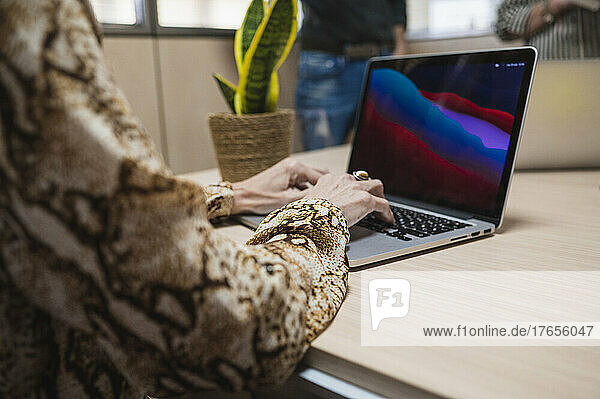 Close up of senior woman hands typing on laptop in an office.