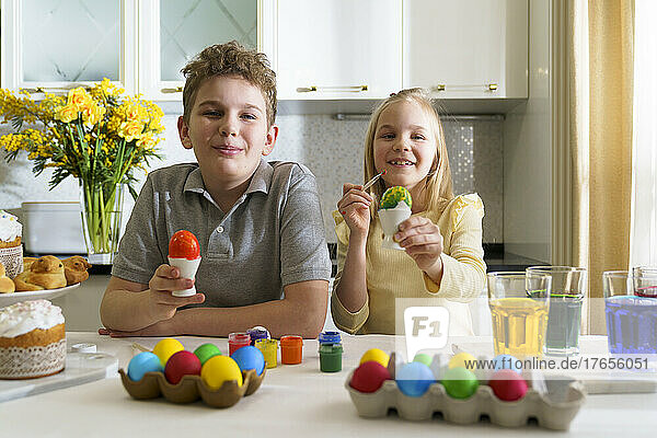 Laughing brother and sister paint Easter eggs.