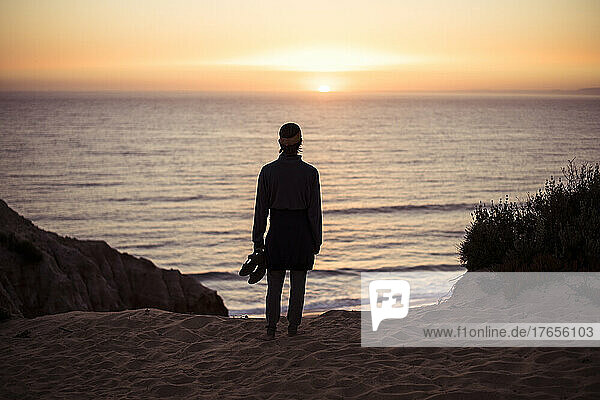 Person looks out onto sunset over ocean from sand dunes