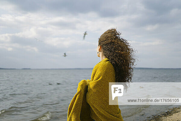 a woman stands on the shore of the lake covered with a yellow cape