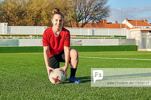 A female soccer player poses with a soccer ball looking at the camera
