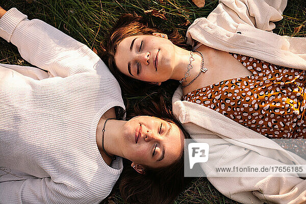 Overhead view of two happy young women lying on grass with eyes closed