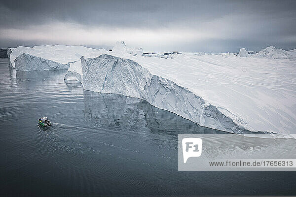 small boat sailing in front of extreme icebergs from aerial view