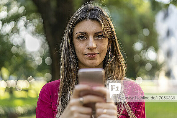 A woman using her smartphone outdoors. She is looking at the camera.