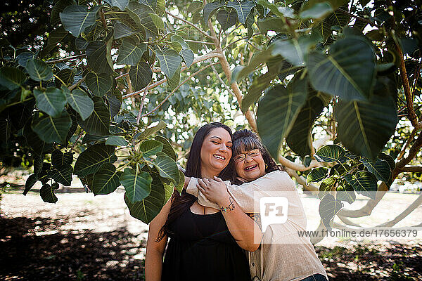 Mom Hugging Daughter at Park Surrounded by Trees in San Diego