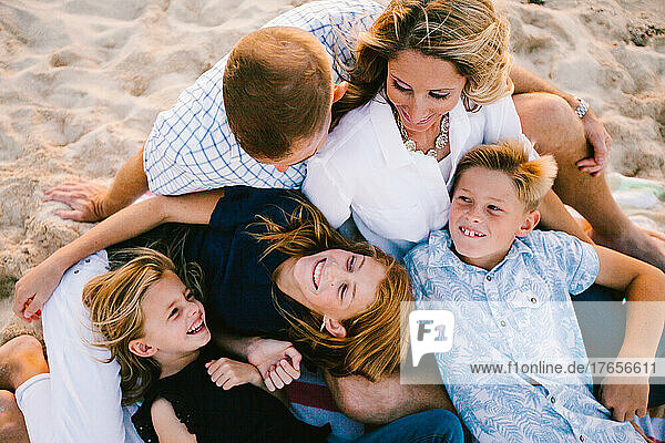 Blond and white family snuggles and laughs on beach with golden light