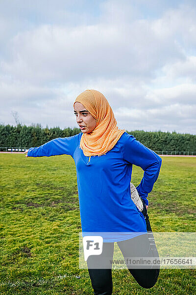 Ethnic woman doing quad stretch exercise on sports field