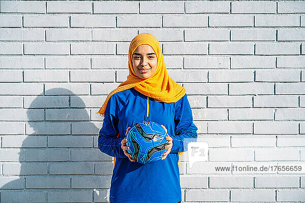 Ethnic woman in hijab standing with football ball