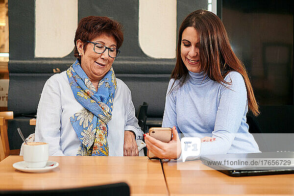 Mature woman and young woman look at a mobile phone in a coffee shop