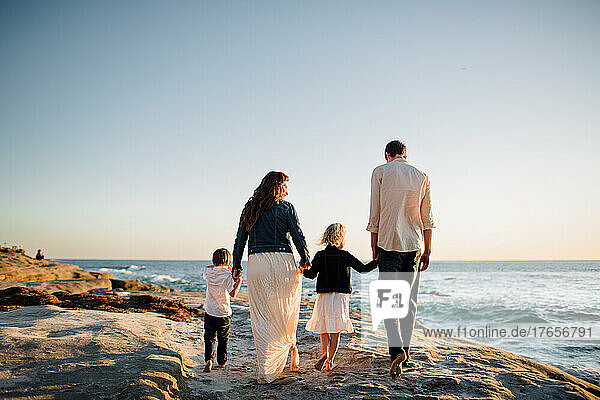 Family of Four Walking Along Cliff on Beach at Sunset in San Diego