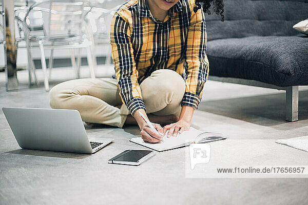 young Afro woman working from home sitting on floor with her laptop