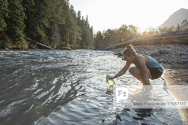 A woman filling a water bottle from the Hoh River.