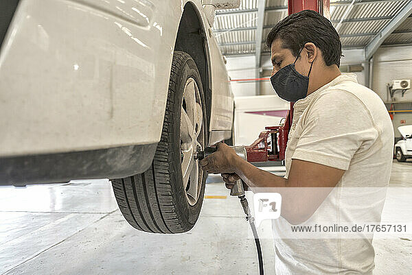 Latin male mechanic removing a white car's wheel with an impact wrench