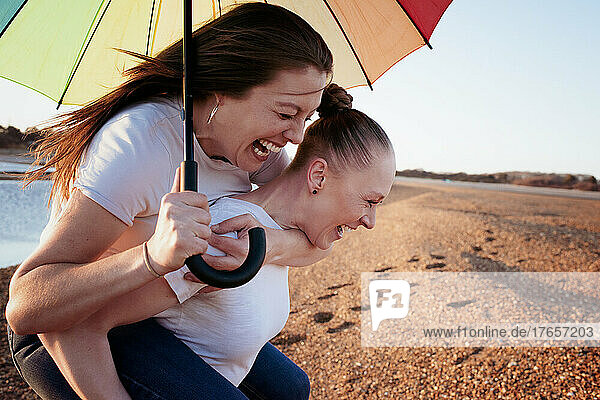 lesbian couple holding pride umbrella laughing at the beach