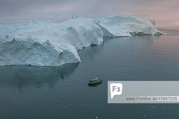 small boat sailing in front of extreme icebergs from aerial view