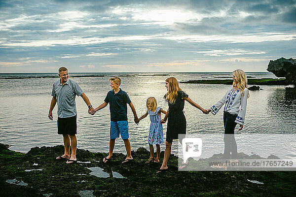 Blond and white family of 5 walks hand in hand by ocean on vacation