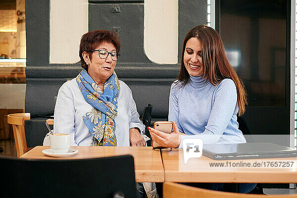 Mature woman and young woman look at a mobile phone in a coffee shop