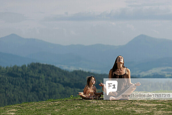 Mother in pose of lotus in mountains with little daughter meditating