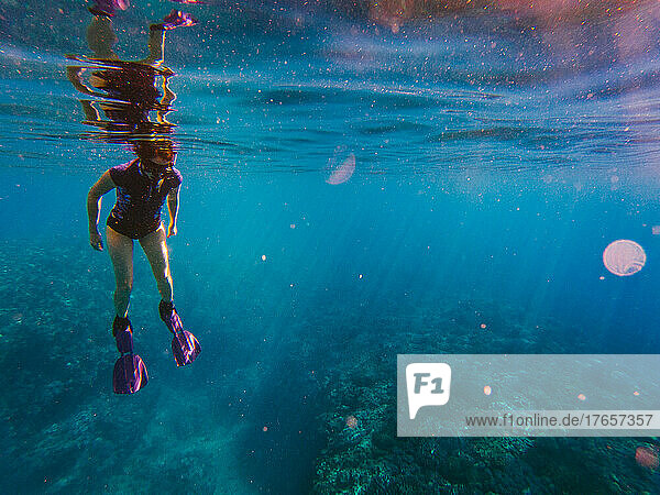 Woman in fins and snorkel gear in blue ocean with sunlight streaming