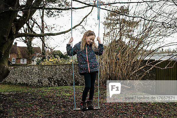 girl happily swinging on a swing in her garden in winter