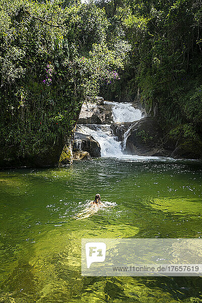 Beautiful view to woman swimming on green pool on rainforest waterfall