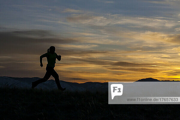 A woman runs at sunset with mountains in the background