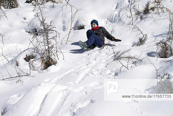 Boy slides down from the snow slope. Enjoying winter sledding time
