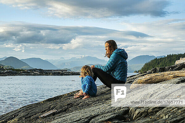 A mom sits with young child on a rock overlooking big bay