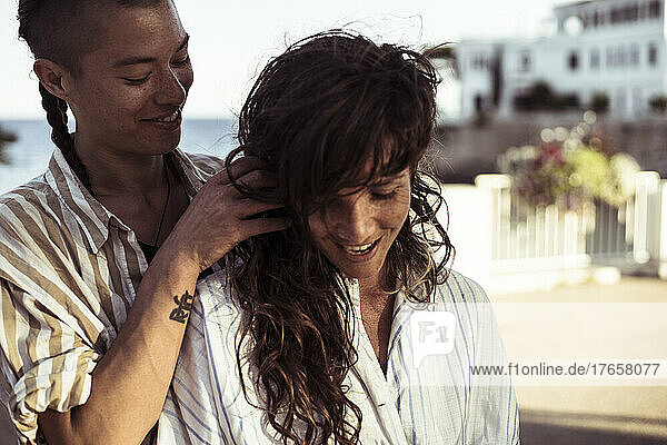 happy queer female couple smile affectionately by Mediterranean sea