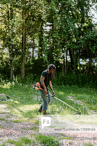 Black man using a weed wacker on a sunny summer day in Bridgeport  CT