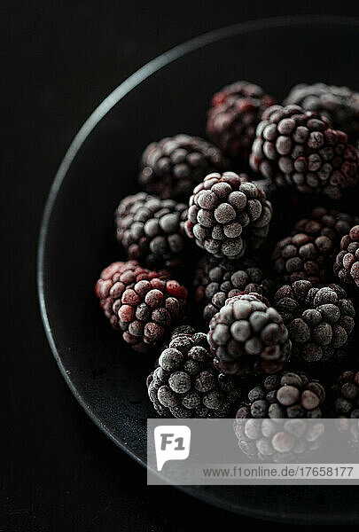 Close up of a black bowl of frosty frozen blackberries.
