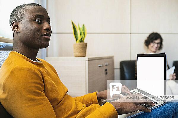 Black young man typing on laptop in an office.