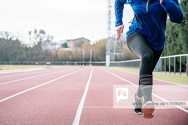 Active woman practicing sprint run on racetrack