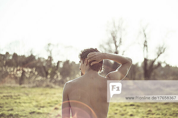 Back on topless young fit man in golden afternoon light on grass field