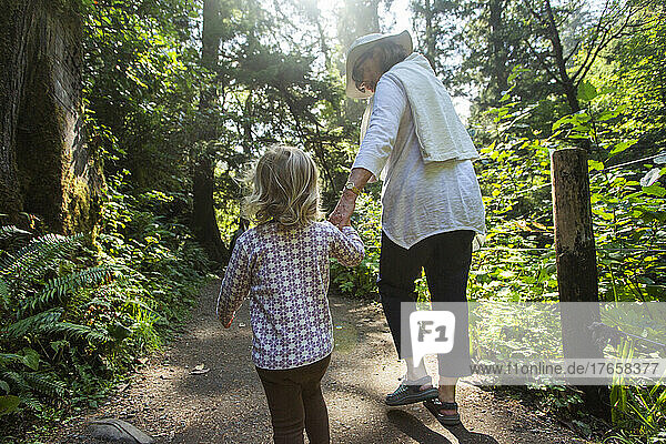 A grandmother holds her grandchild's hand on forest trail