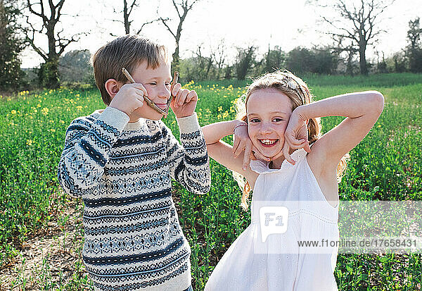 siblings playfully pulling faces together outside in a flower field