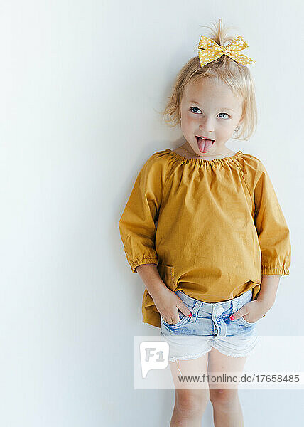 cute little girl with yellow bow and top on a white wall