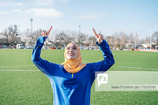 Smiling Arab female raising forefingers on sports field