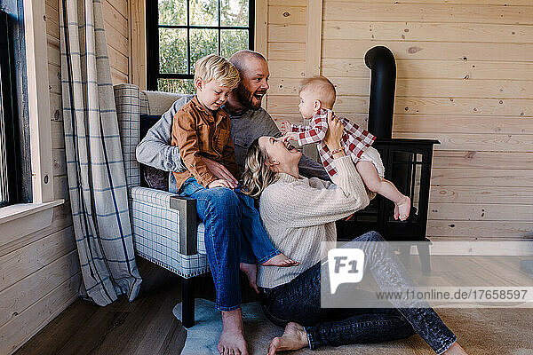 Young Caucasian family laughs and plays near fireplace in cabin