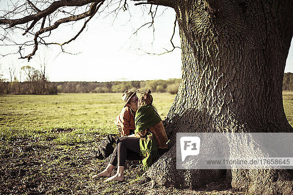 Romantic androgynous couple kiss under and large tree in grassy field