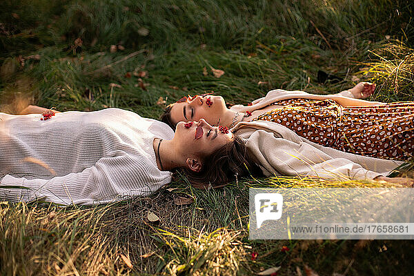 Two young women relaxing while lying on grass during autumn